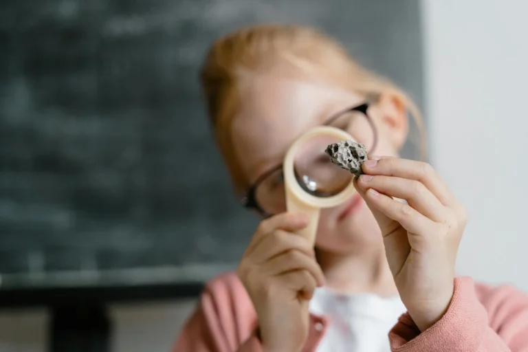 A young girl exploring a rock sample with curiosity using a magnifying glass indoors.