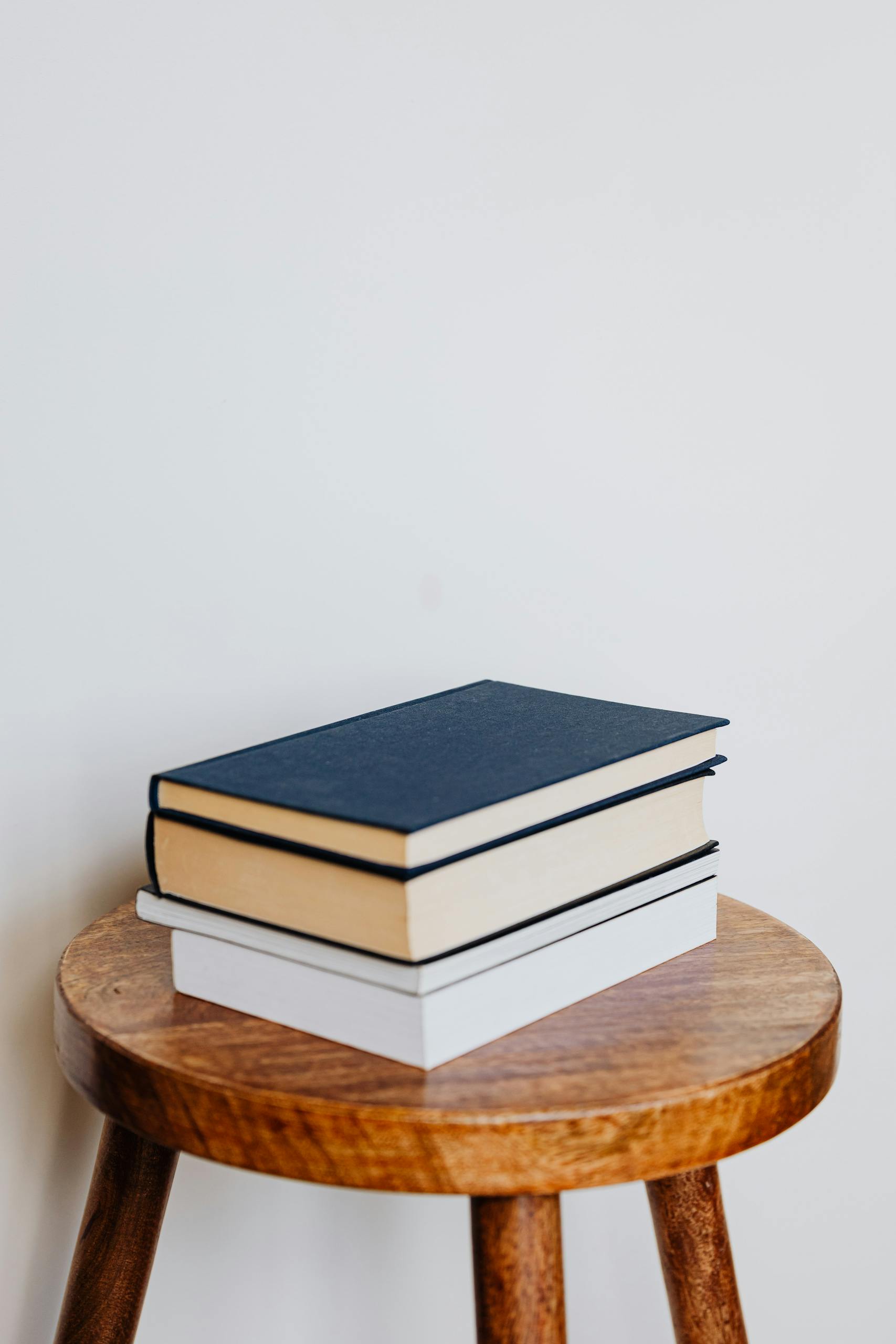 A stack of hardcover books on a wooden stool against a plain background, perfect for educational themes.